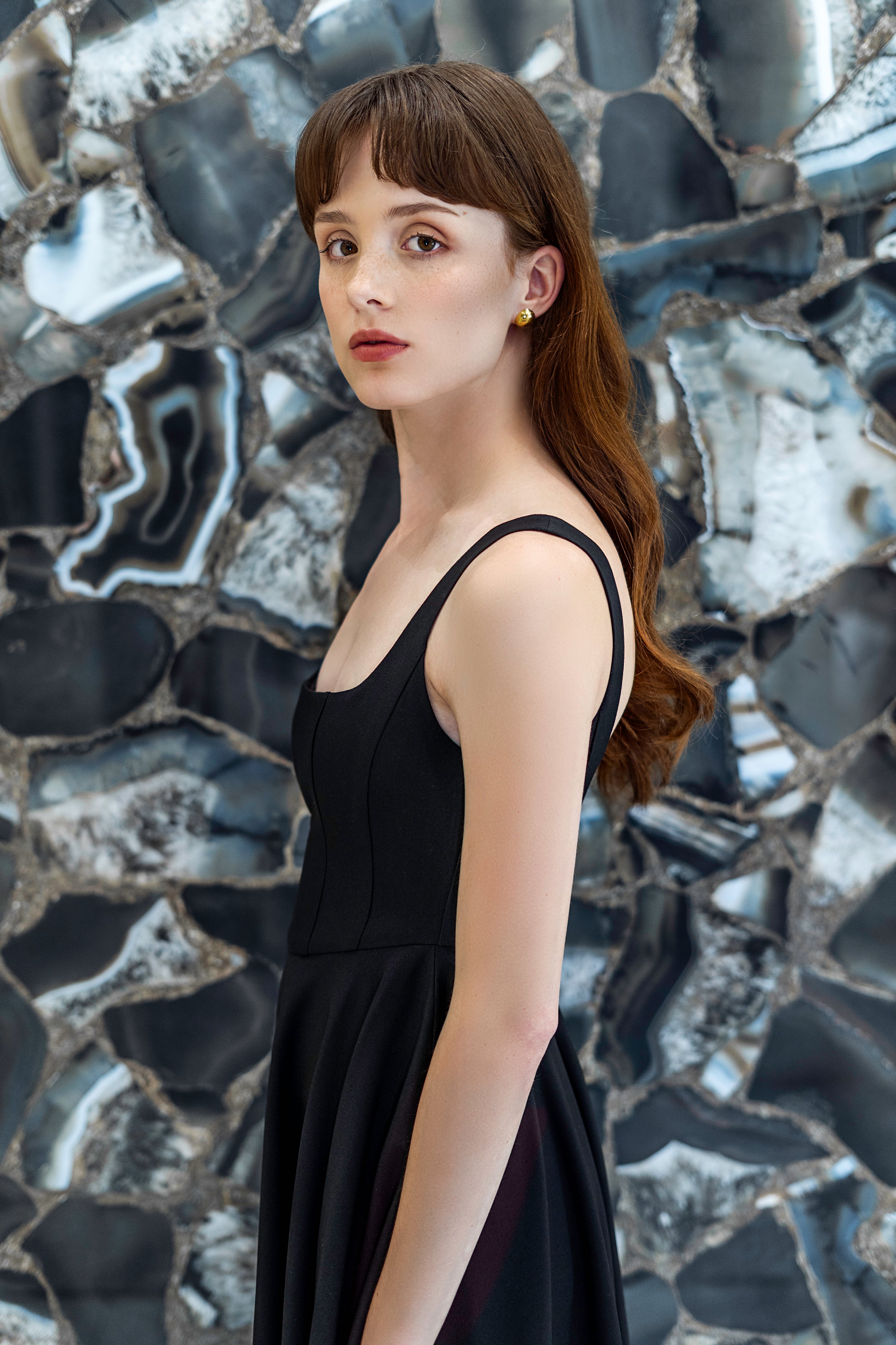 Woman in a black dress standing against a mosaic wall.